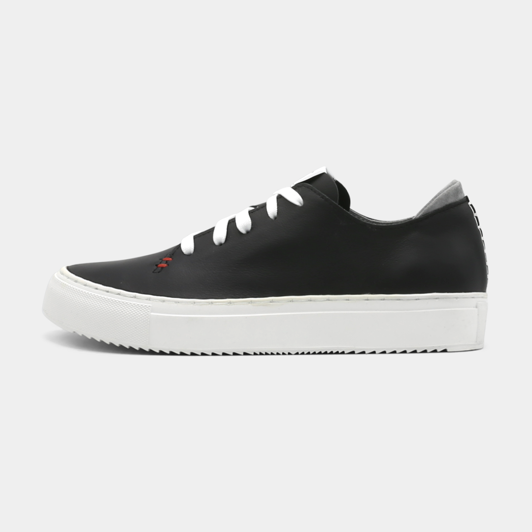 A black colored low-top sneaker with a white sole and laces, lateral view.
