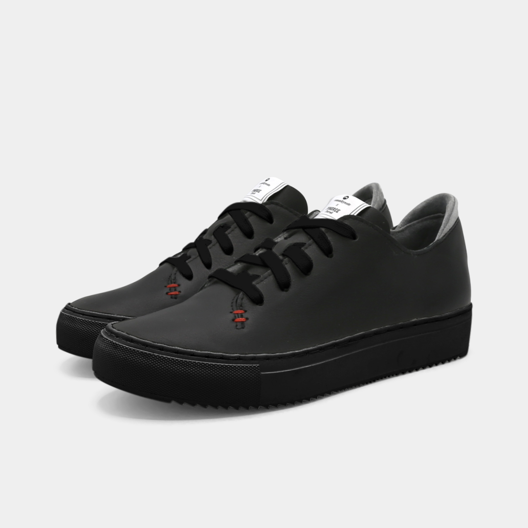A black colored low-top sneaker with a black sole and laces, quarter view.