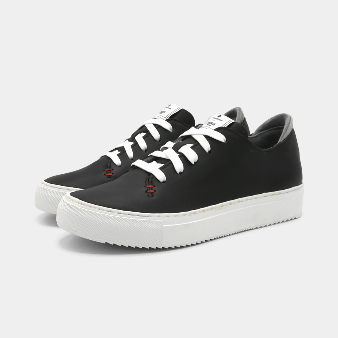A black colored low-top sneaker with a white sole and laces, quarter view.