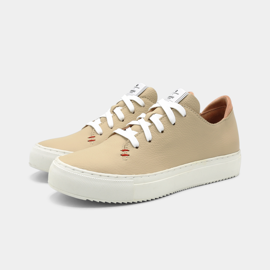 A cream colored low-top sneaker with a white sole and laces, quarter view.