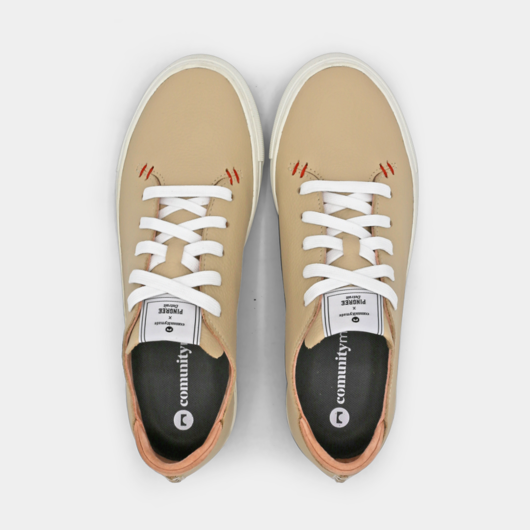 A cream colored low-top sneaker with a white sole and laces, top view.
