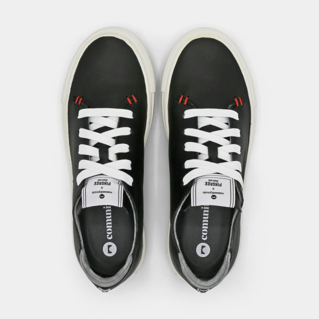 A black colored low-top sneaker with a white sole and laces, top view.