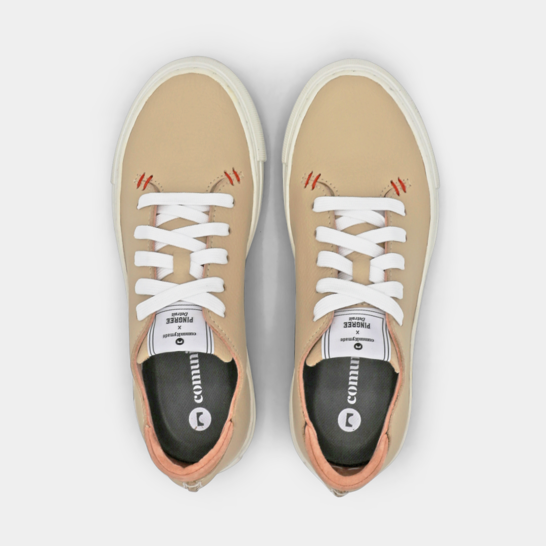 A cream colored low-top sneaker with a white sole and laces, top view.