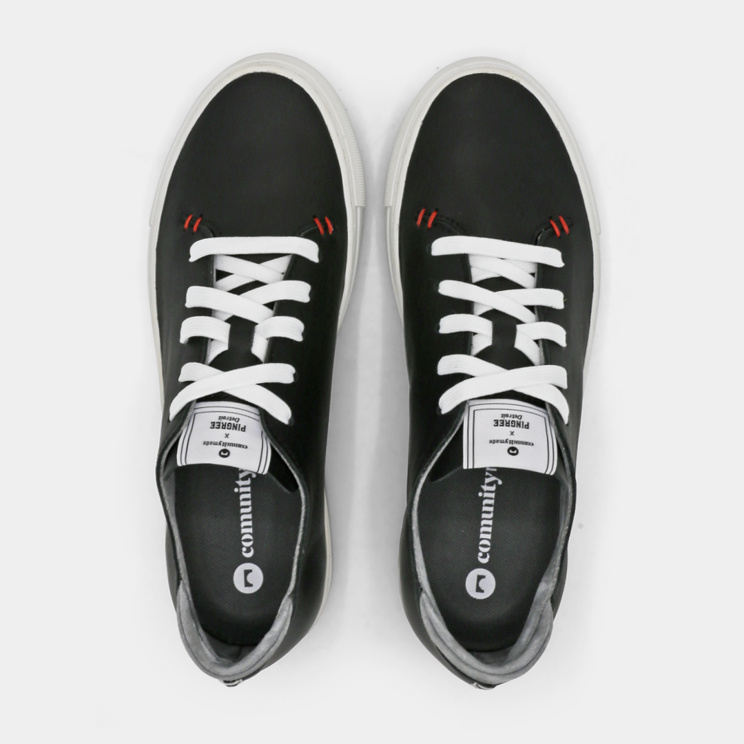 A black colored low-top sneaker with a white sole and laces, top view.