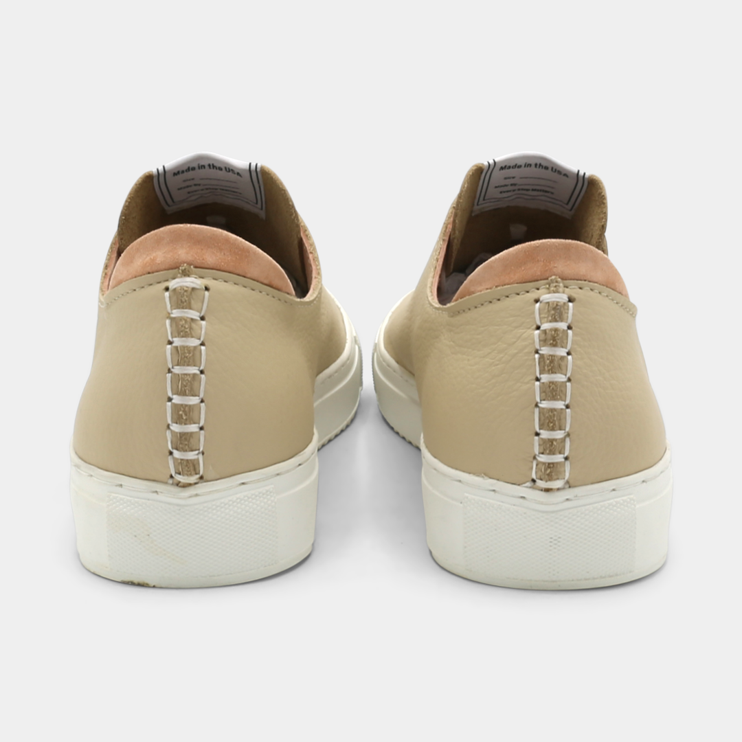 A cream colored low-top sneaker with a white sole and laces, back view.