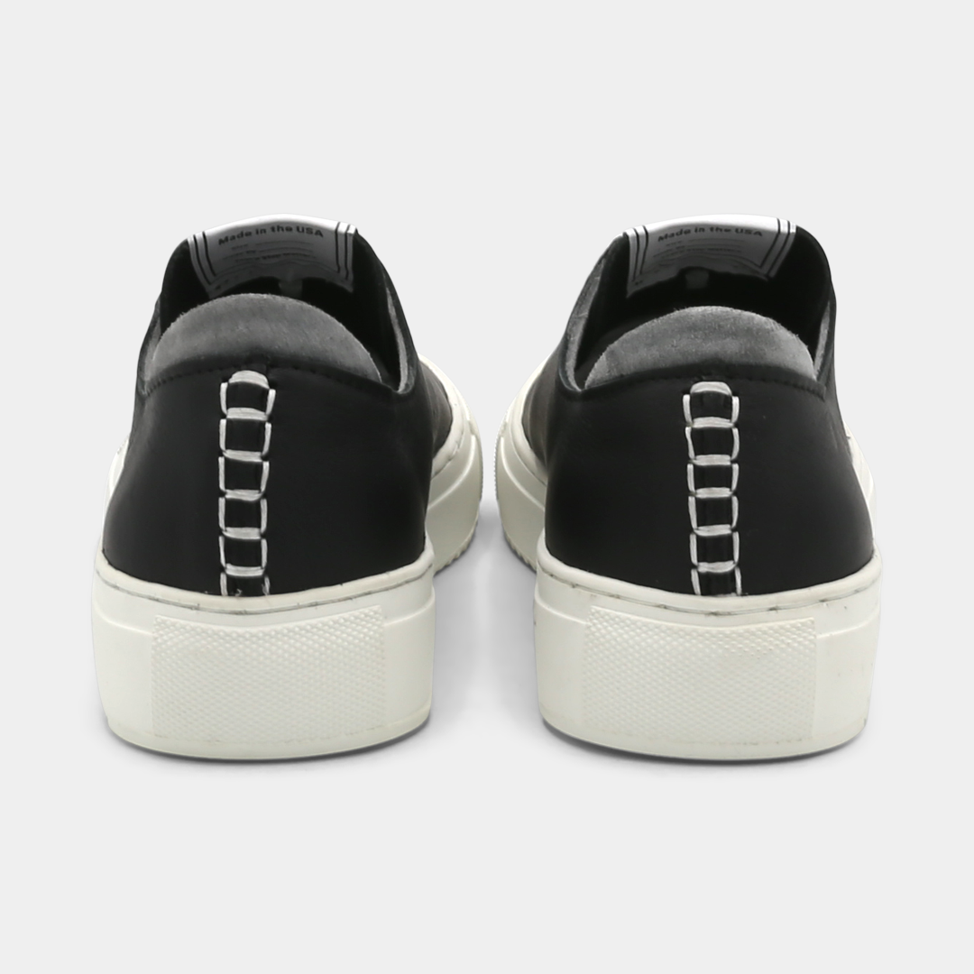 A black colored low-top sneaker with a white sole and laces, back view.