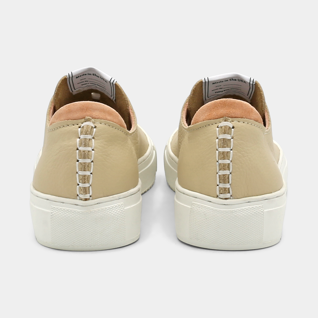 A cream colored low-top sneaker with a white sole and laces, back view.