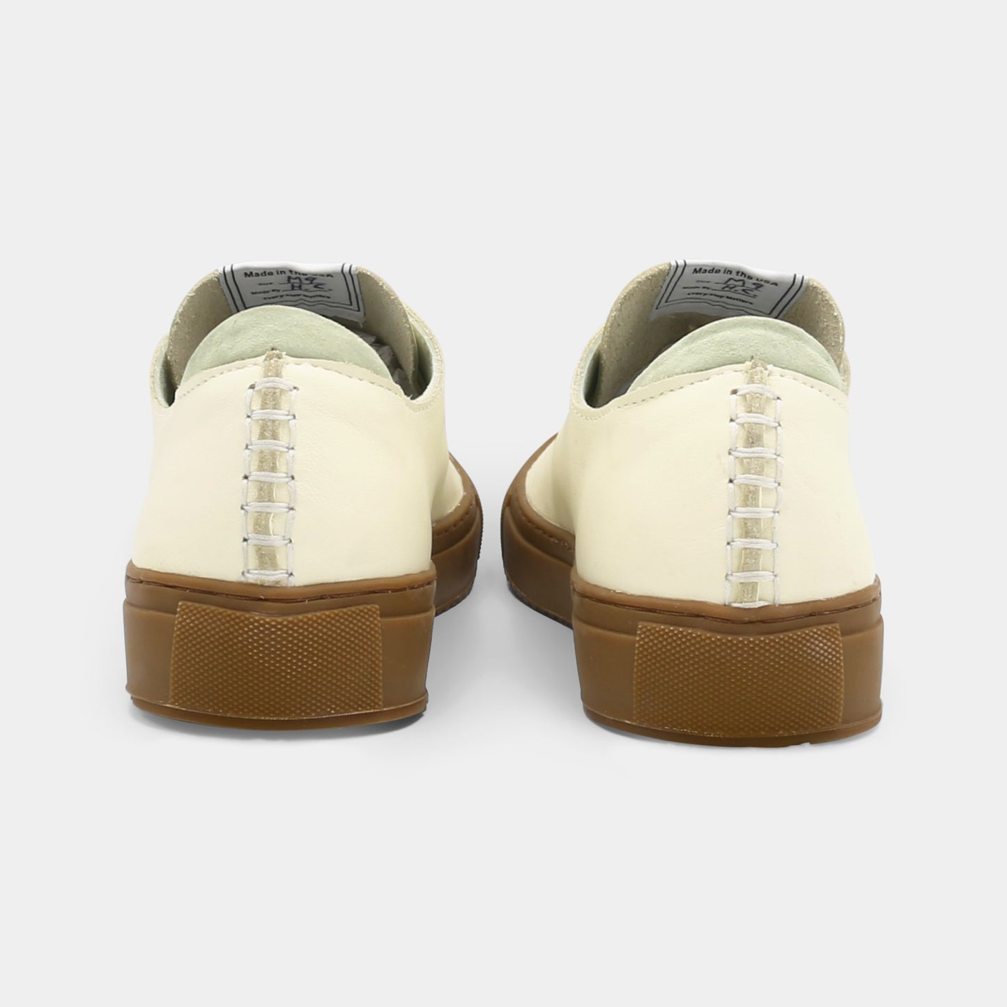 A latte colored low-top sneaker with a brown sole and white laces, back view.