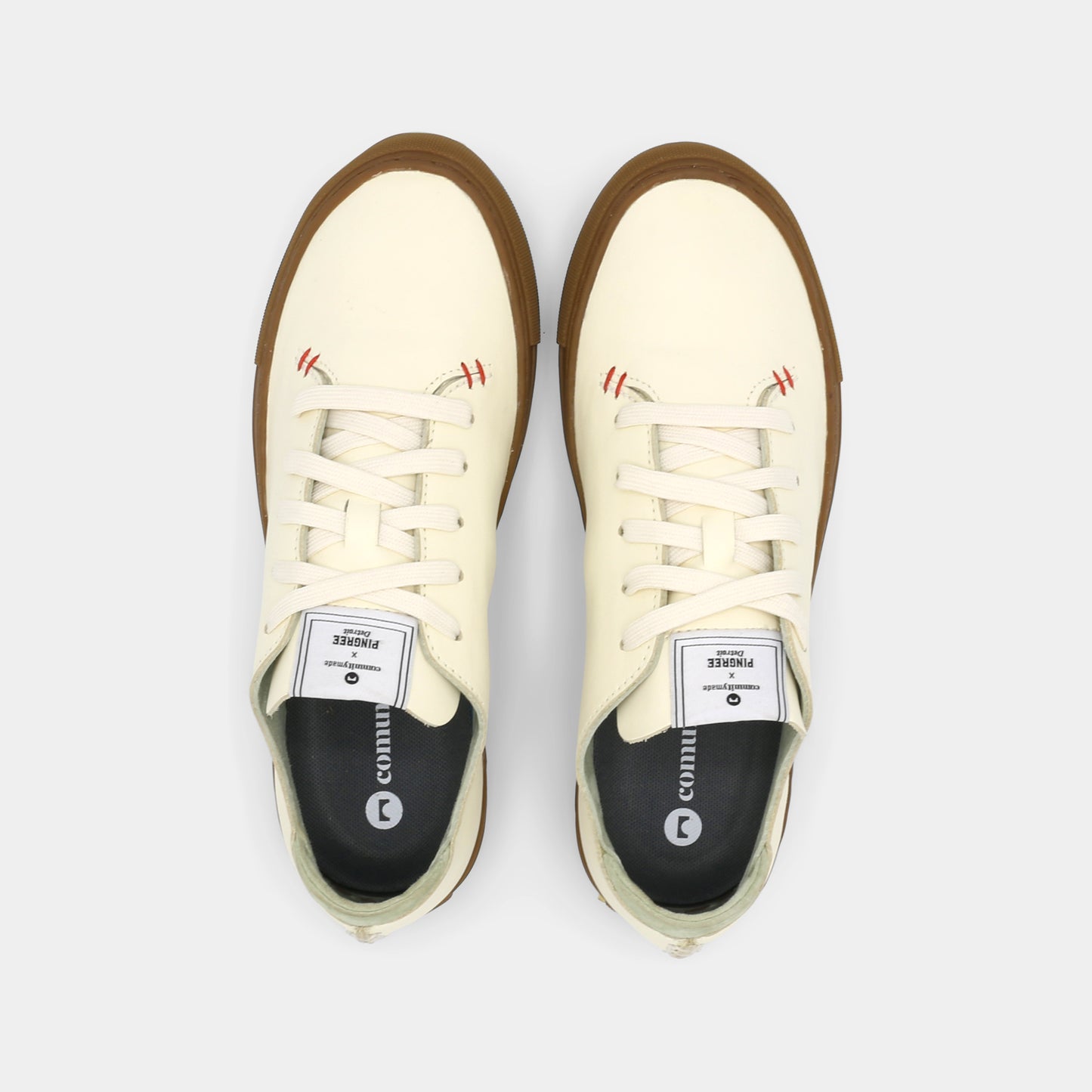 A latte colored low-top sneaker with a brown sole and white laces, top view.