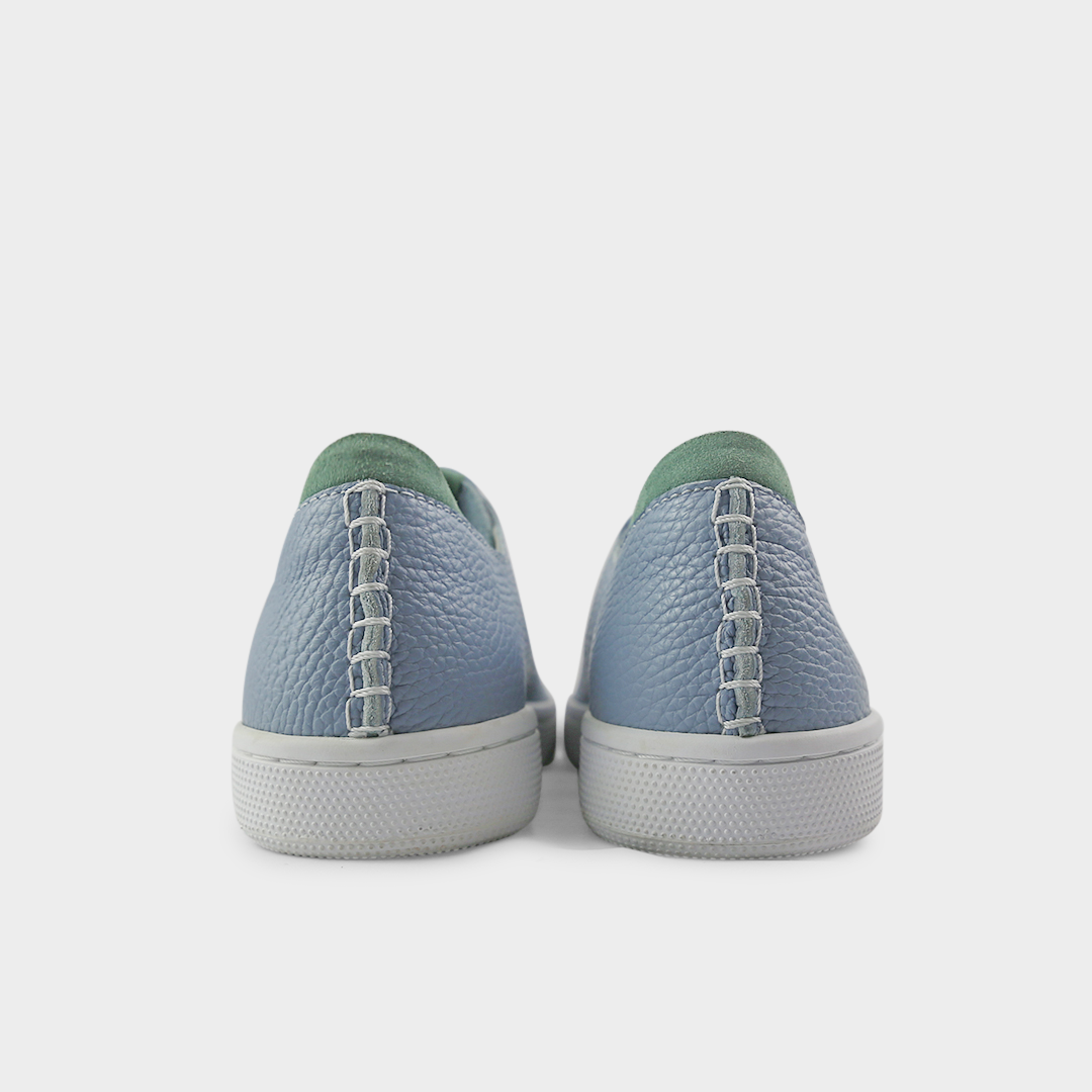 A rearview shot of a pair of sky blue leather sneakers with white accent stitching on the heel, a white rubber cupsole sole and a green accent on the heel and tongue.