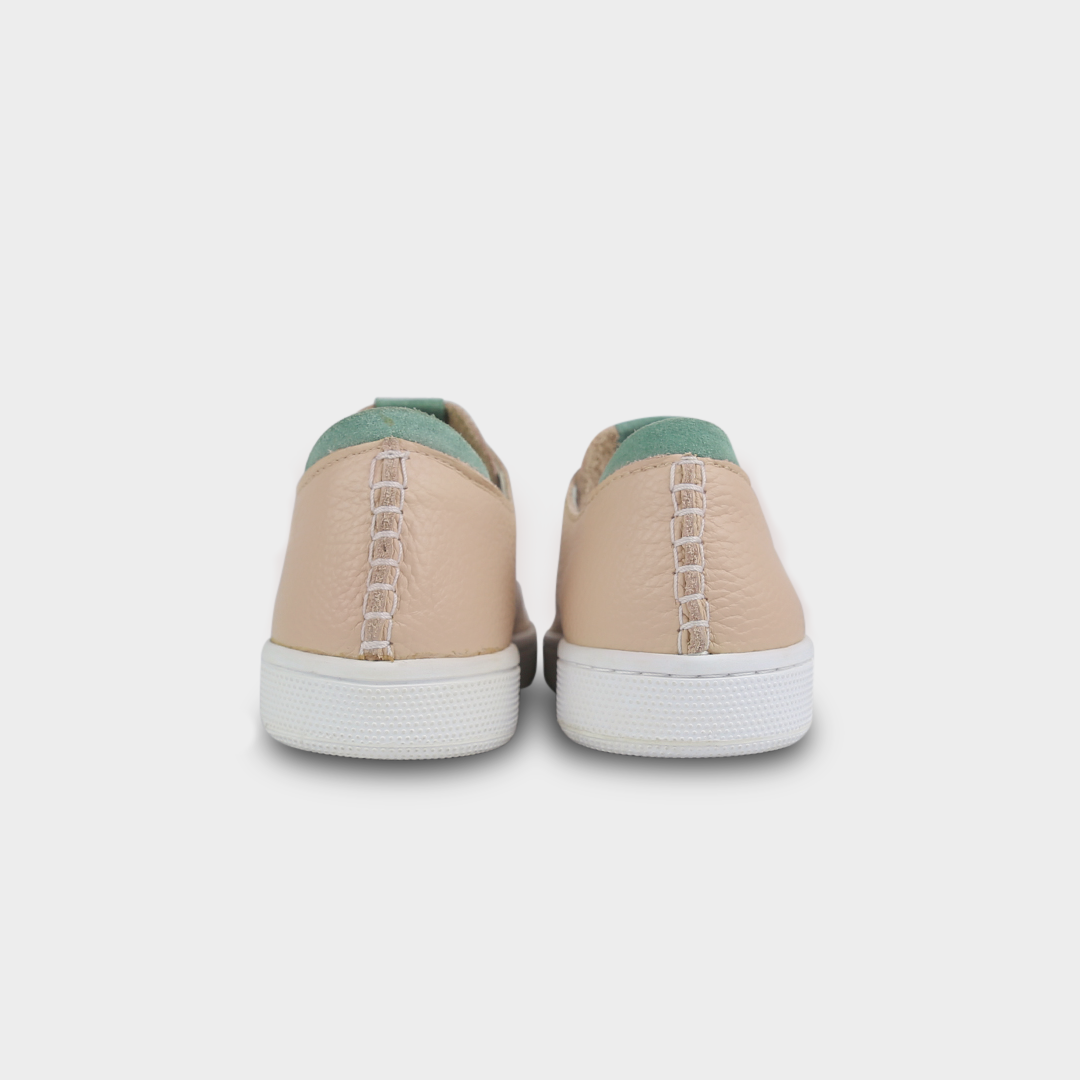A rearview shot of a pair of nude beige leather sneakers with white accent stitching on the heel, a white rubber cupsole sole and a green accent on the heel and tongue.