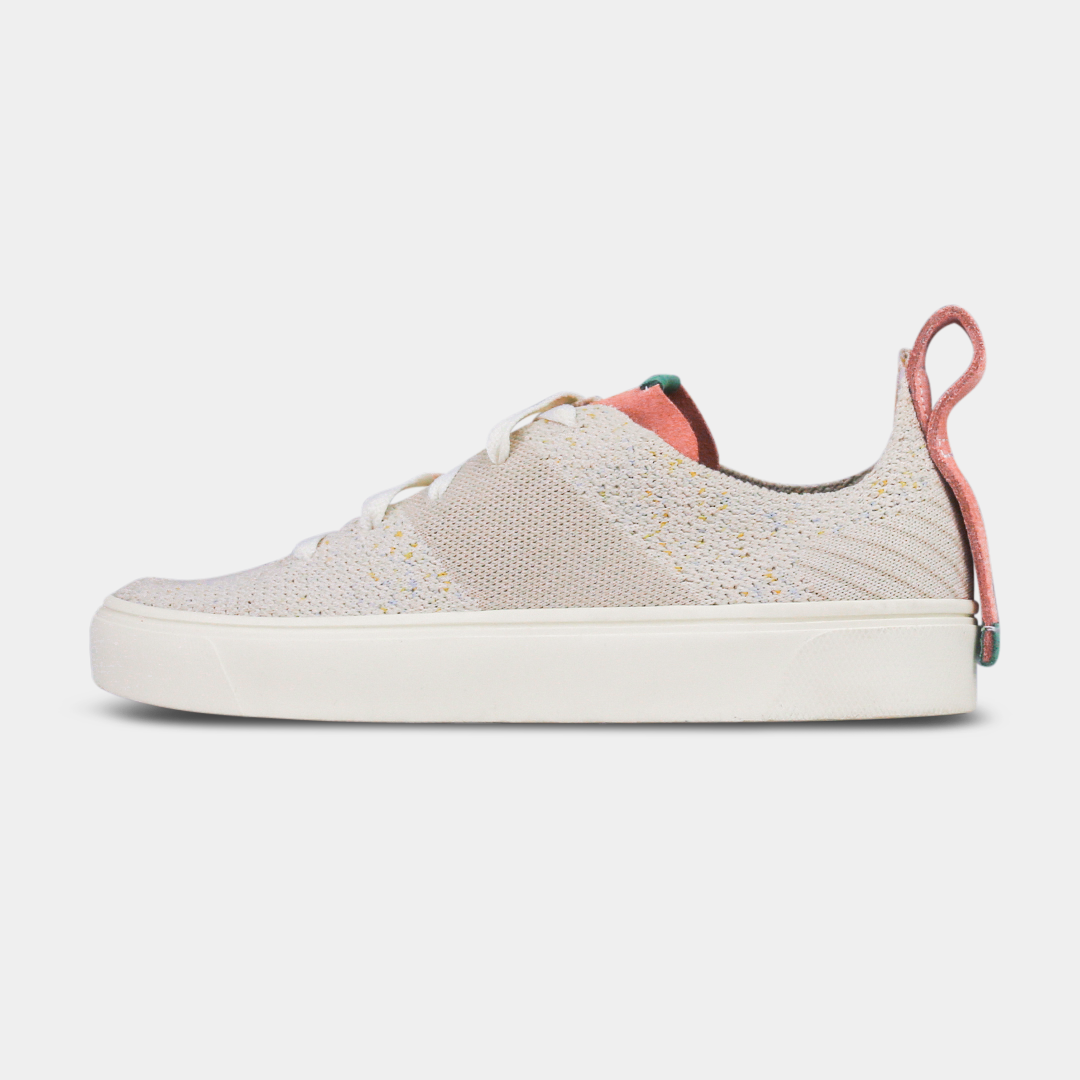 A pair of women's sneakers with a knit upper in a beige color, featuring premium leather accents and a lace-up closure system.A pair of off-white knitted sneakers with light pink speckles. The shoes have white laces, a pale pink tongue, and a pink and white heel loop. The insoles are dark green with a white text logo and a circle.