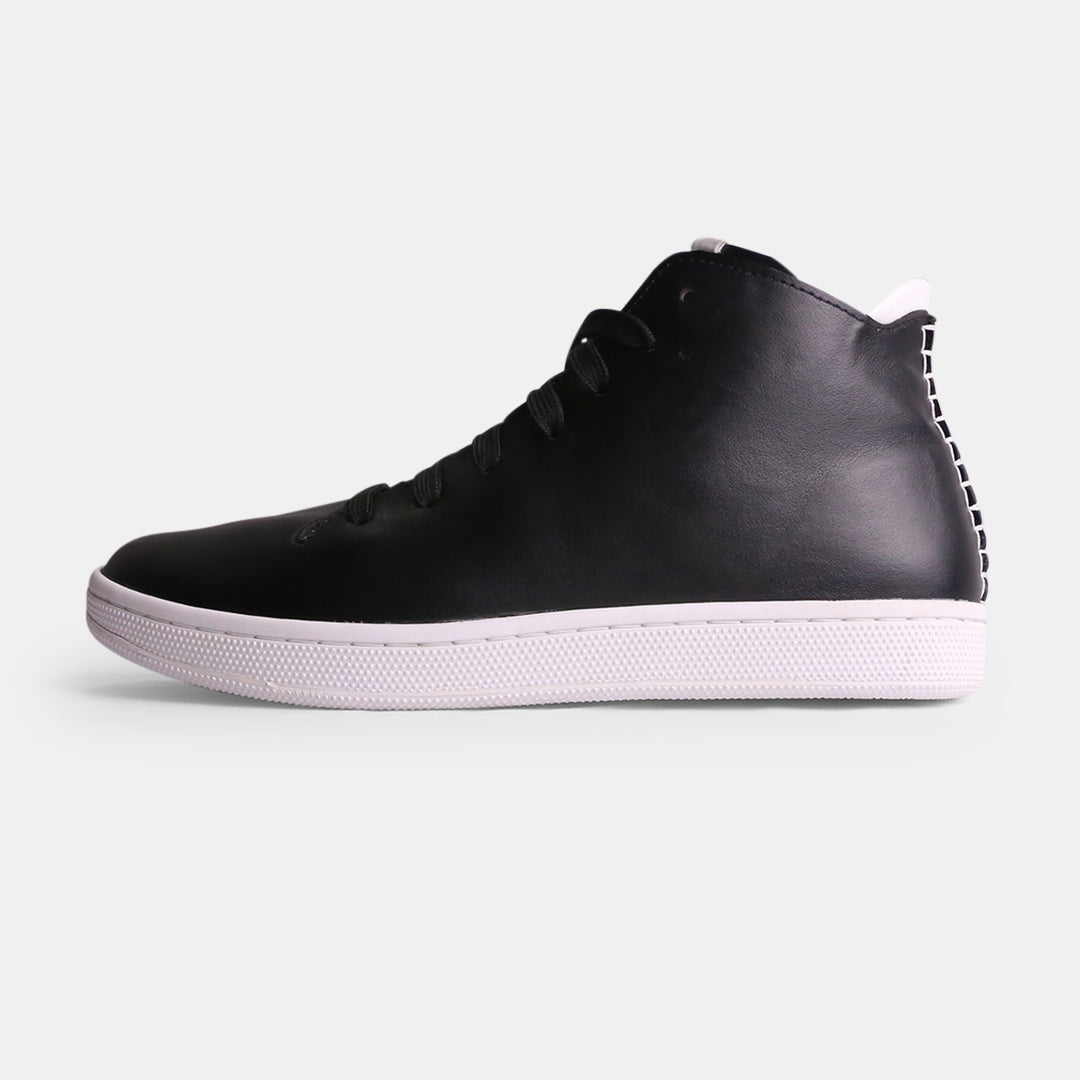 Side profile of a black leather mid-top sneaker with a white cupsole and white accent stitching on the heel