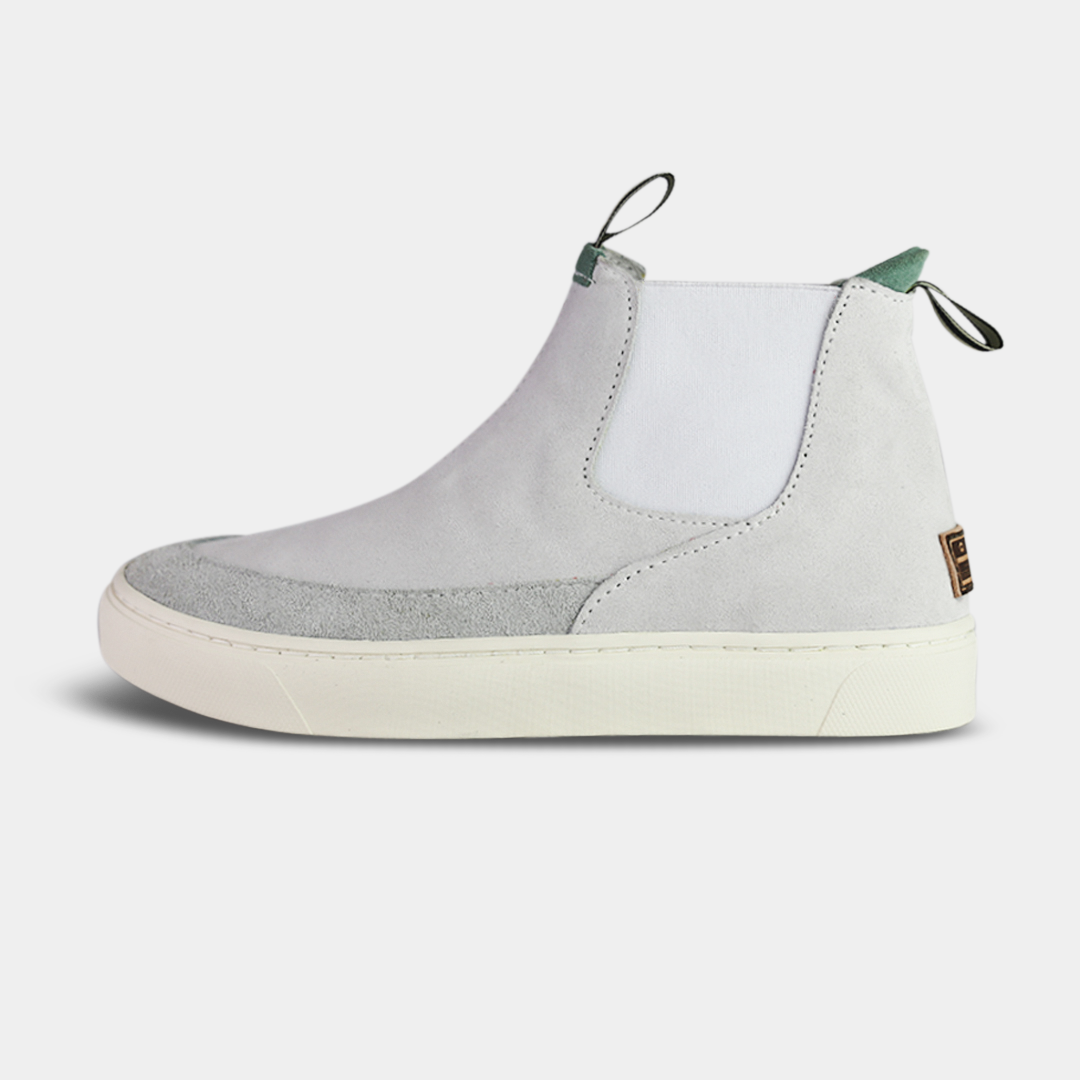 A pair of light gray suede boots with white soles. The boots feature a mint green elasticated panel and a striped brown and black pull tab at the back of the ankle. The toe area is a different texture of suede with a visible seam