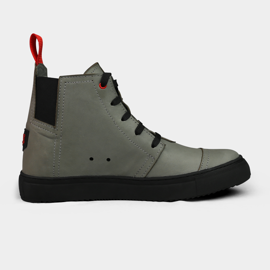 A product shot of the side of a pair of grey high-top shoes. The shoes are made of grey leather, with a black sole and a red loop on the back of the ankle. A red square with