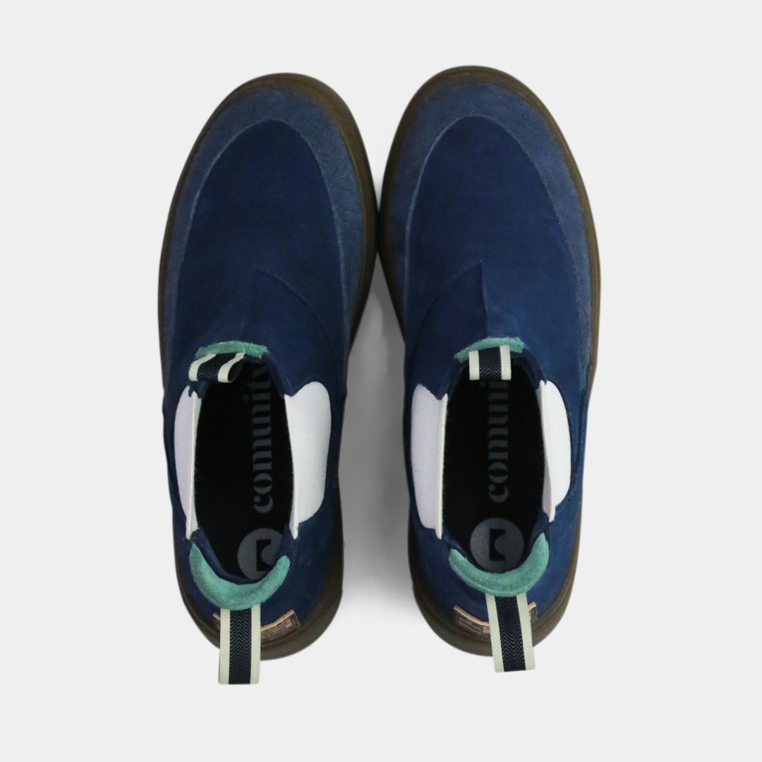 A pair of dark blue suede ankle boots with a brown rubber sole. The boots feature a light brown leather logo tag with