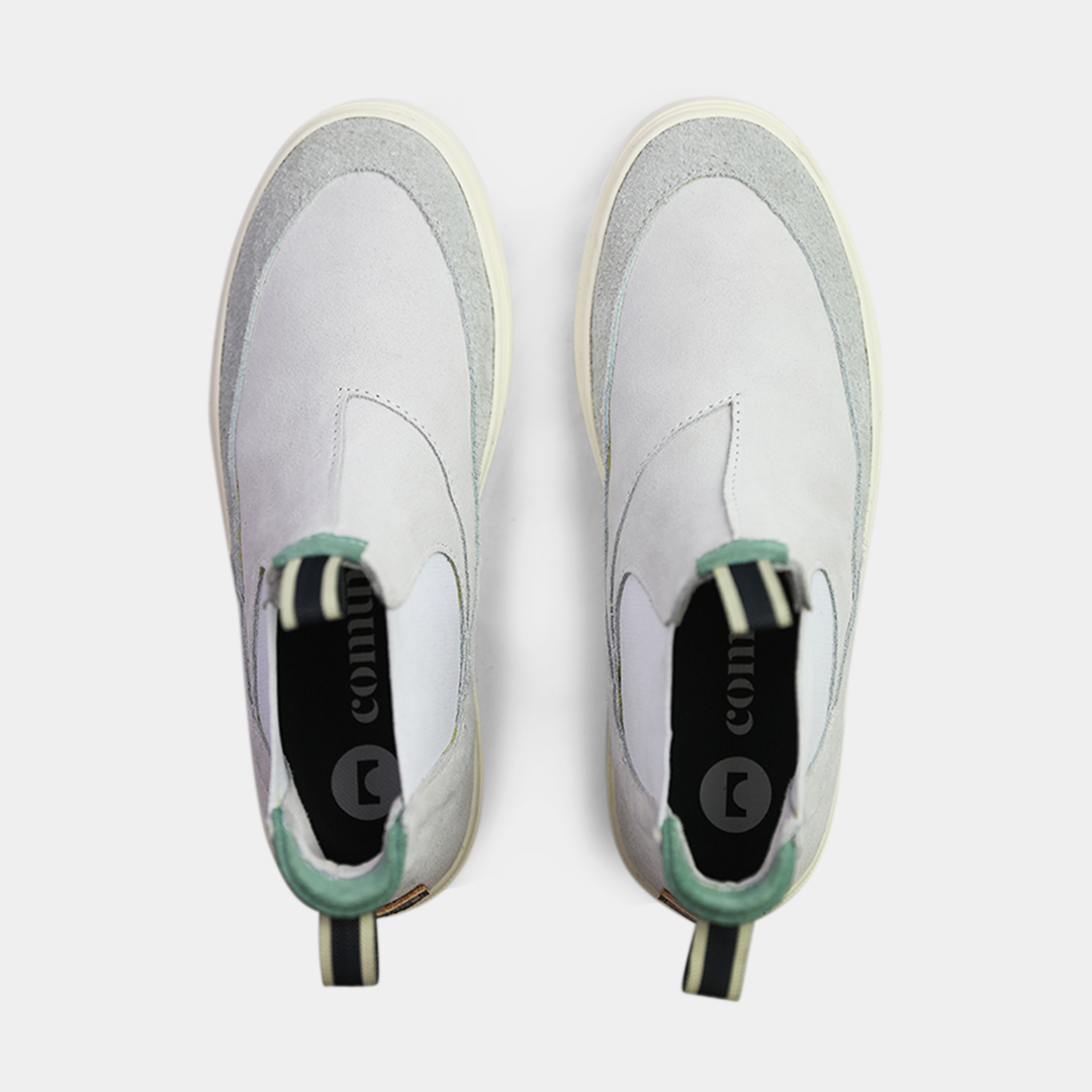 A pair of light gray suede boots with white soles. The boots feature a mint green elasticated panel and a striped brown and black pull tab at the back of the ankle. The toe area is a different texture of suede with a visible seam.