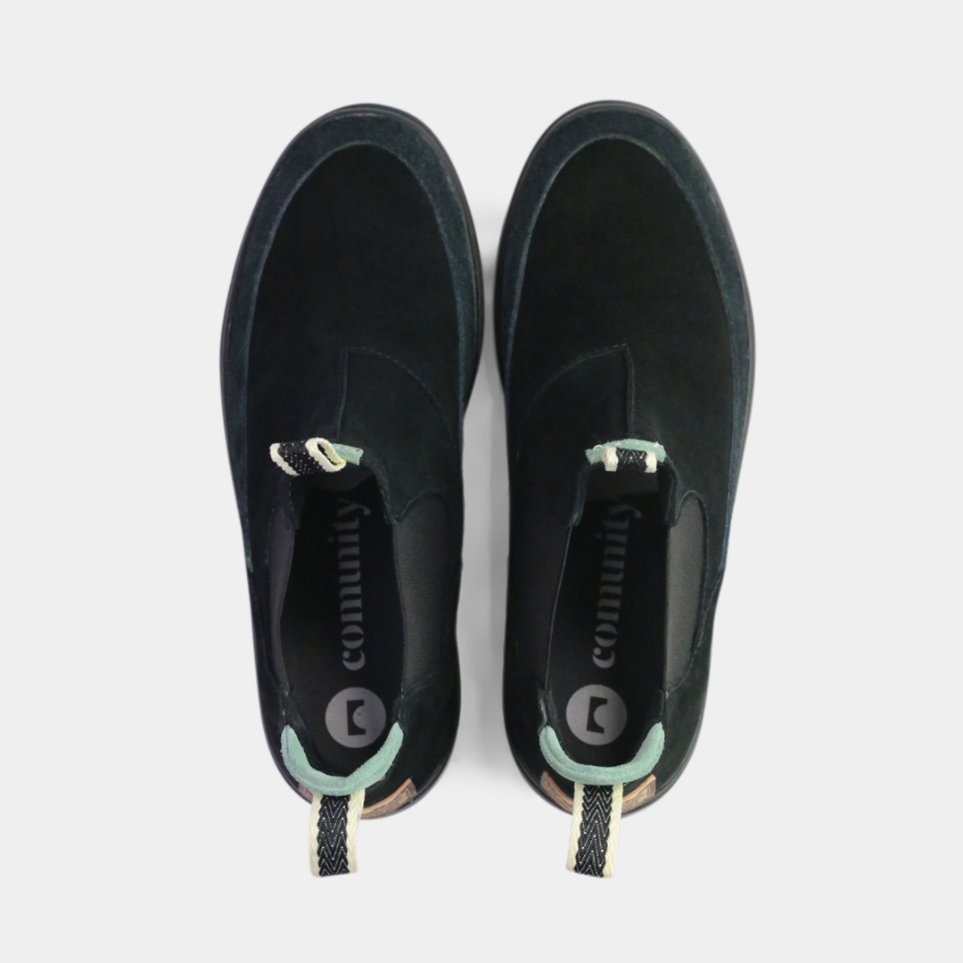 A pair of black suede Chelsea boots. The shoes have black elastic gussets on the side and a striped pull tab at the heel. The black insoles feature a white