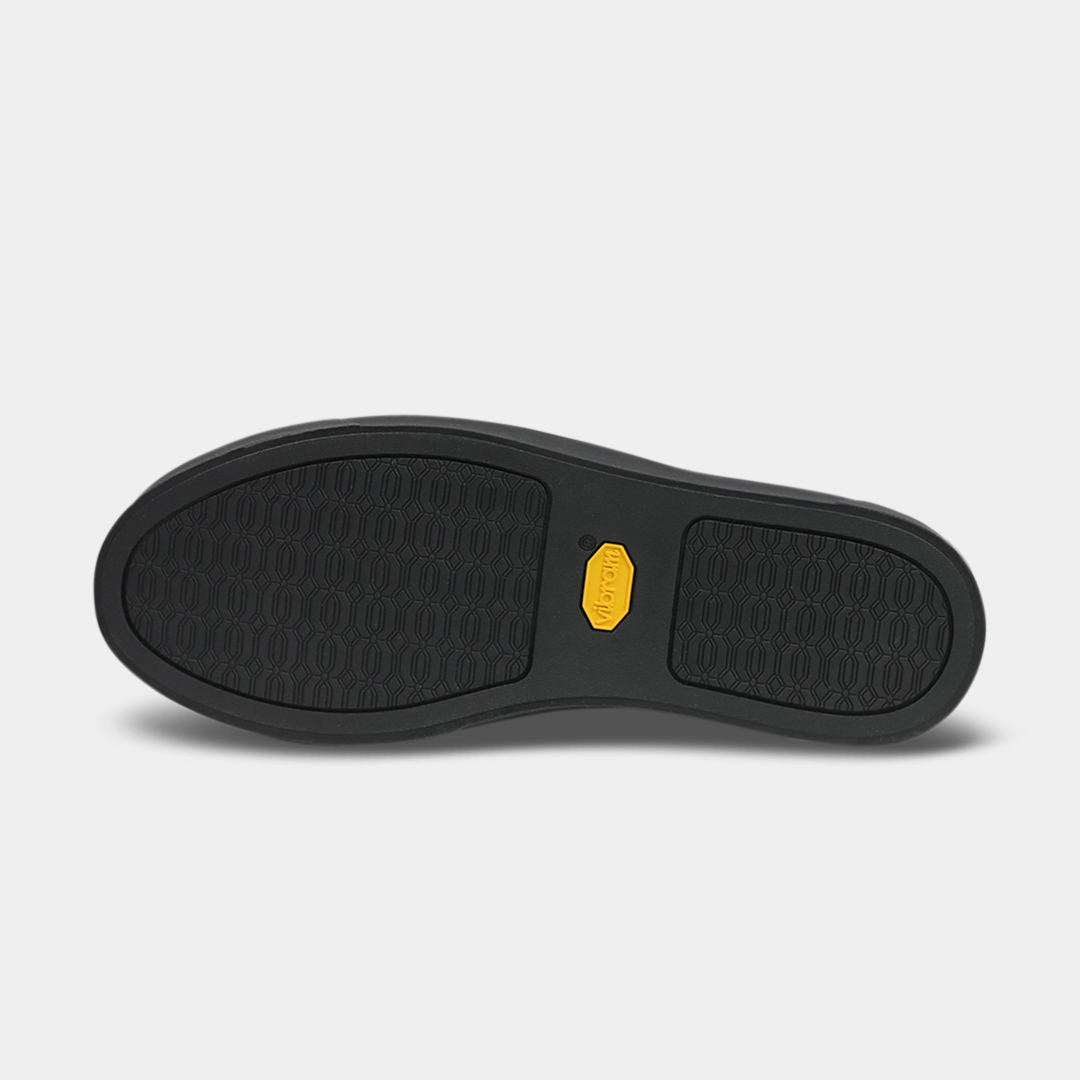 The bottom of a shoe with a black rubber sole. The front and back of the sole have a repeating, circular pattern for grip, with a bright yellow oval logo in the center.