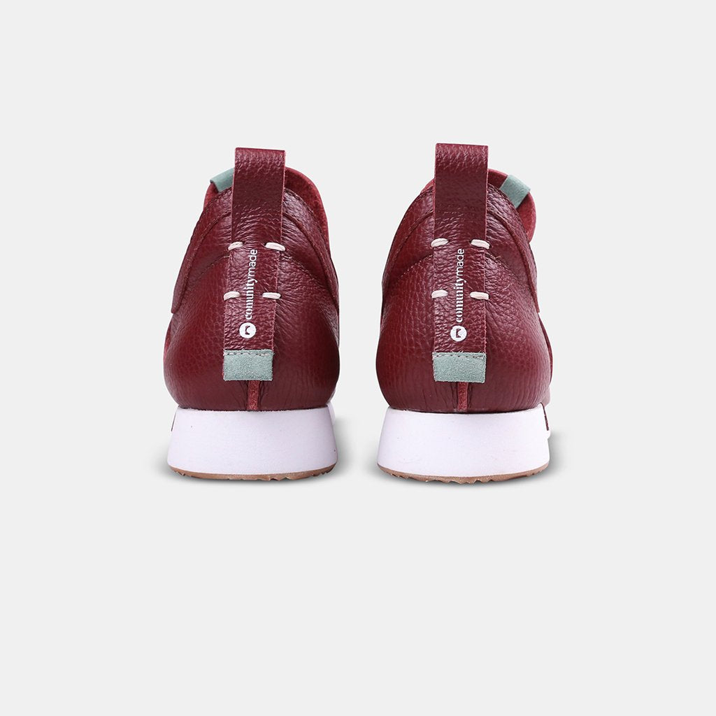 A rear view of two Comunitymade shoes made of a deep burgundy, pebbled leather. They have thick white soles and a leather pull tab on the back of each heel with the words