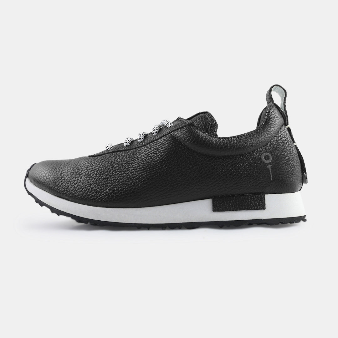 A pair of black pebbled leather sneakers with white soles and black laces with white flecks. The sneakers have a small mint green accent on the tongue and back pull tab. A small black tag with a white square and a faint logo is on the side of the heel.