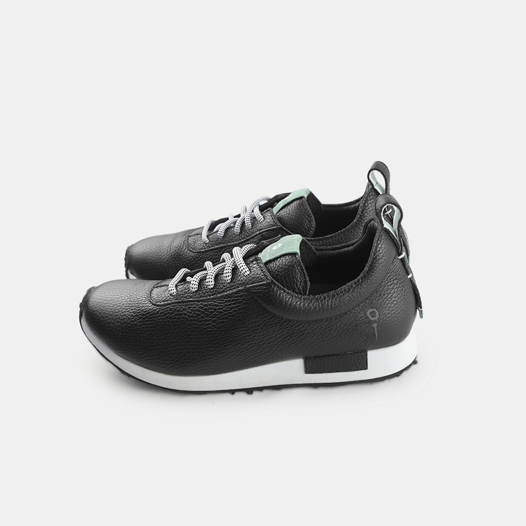 A pair of black pebbled leather sneakers with white soles and black laces with white flecks. The sneakers have a small mint green accent on the tongue and back pull tab. A small black tag with a white square and a faint logo is on the side of the heel.
