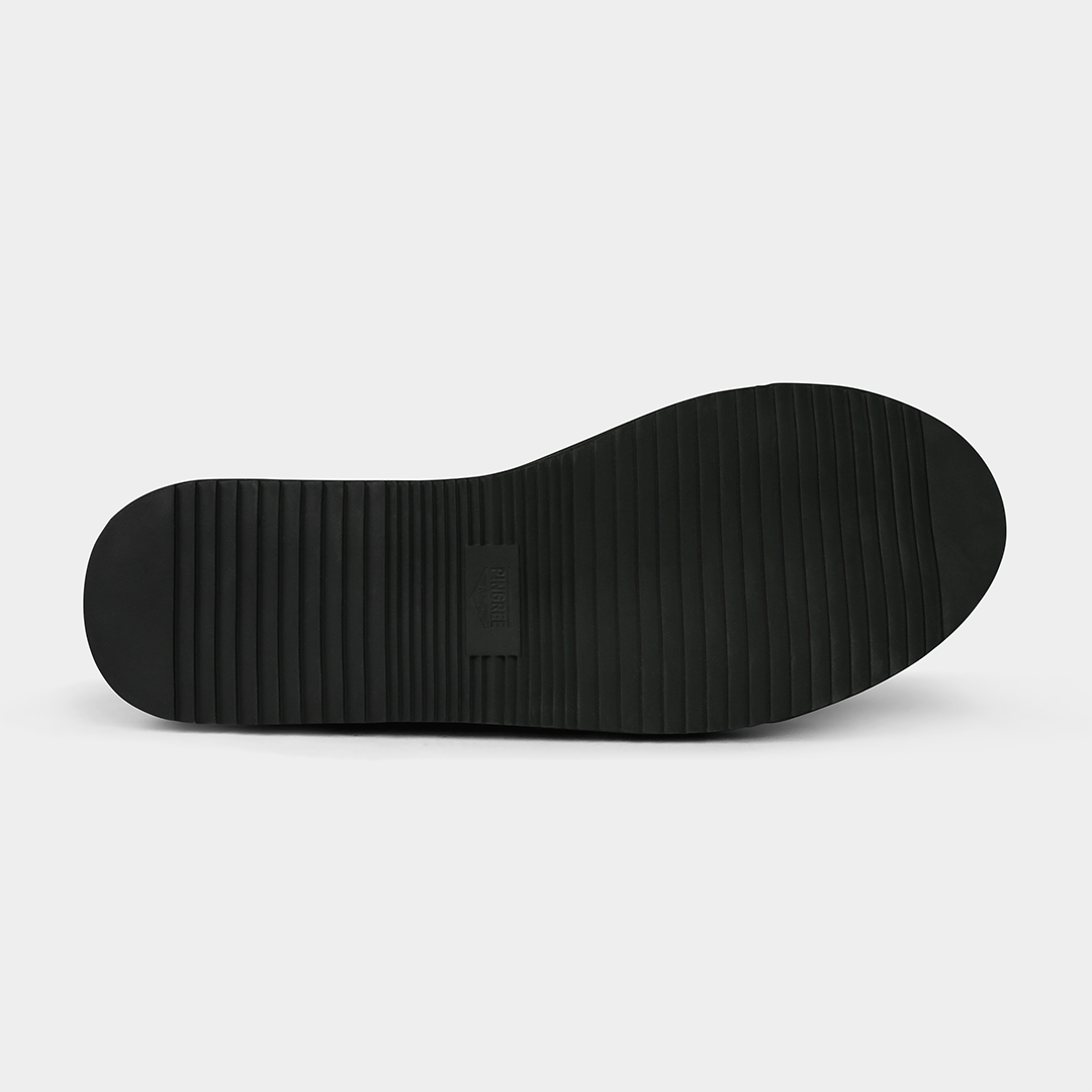 A product shot of the bottom of a shoe. The sole is a solid black with a simple ridged or corrugated tread pattern. A rectangular patch with the word