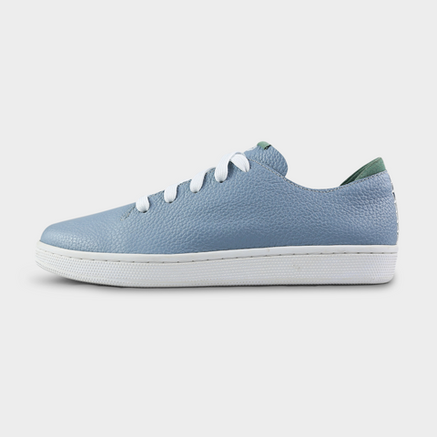 A profile shot of single sky blue leather sneaker with a lace-up closure, featuring flat white shoelaces, a white rubber cupsole and a green accent on the heel.