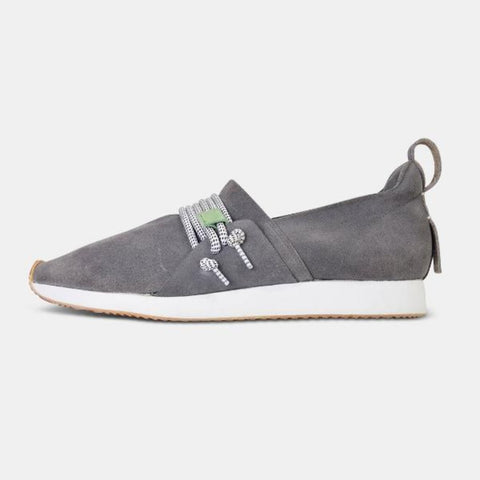 A profile product shot of a single grey suede slip-on shoe. The shoe has a thick white sole with a light brown tread. A thick, speckled black and white rope-like lace is threaded through the side of the shoe and tied in a knot. A small grey leather loop is on the back of the heel. The shoe is on a solid gray background.