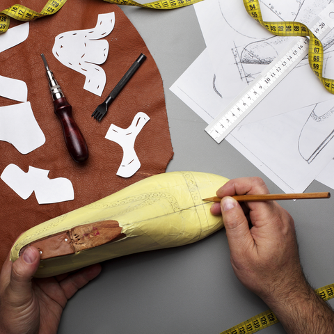 Picture of a shoemaking last form and shoe patterns surrounding it and leather with patterns cut into it